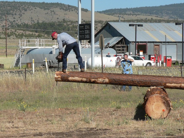Man wit chainsaw balanced on end of log, sawing!