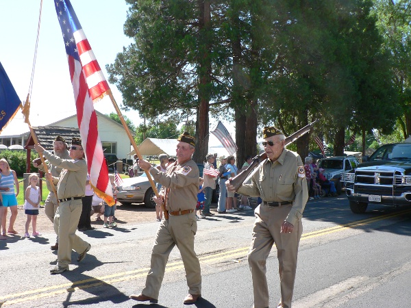 4 men in uniform carry an American Flag. They are leading a parade.