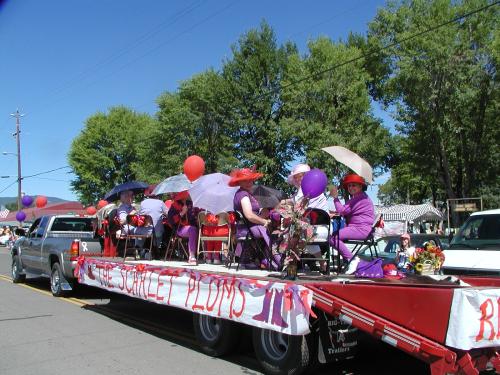 A float labeled "Scarlet Plums" with elegant ladies on board.