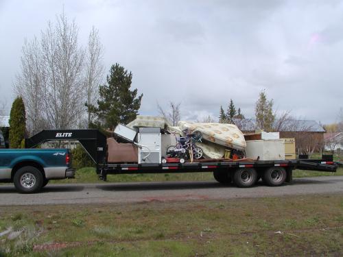 A flatbed trailer piled with old appliences, mattresses, furniture and other junk.
