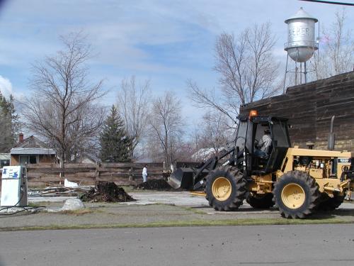 The old gas station (only junk and old pump remaining) gets help from a yellow loader.