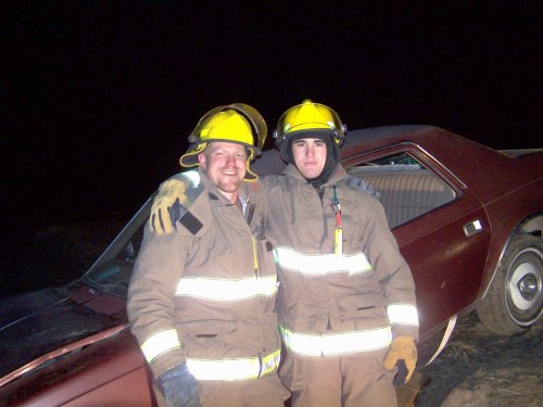 2 firemen smiling in front of wrecked car.  It's a training!