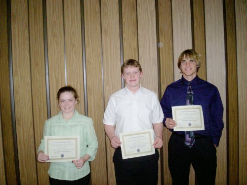 A young lady on the right with 2 young men each holding certificates.