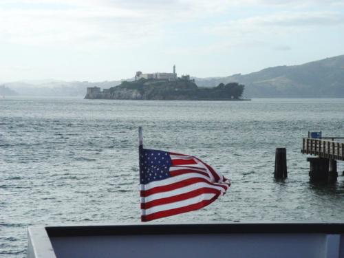 Alcatraz Island behind the American Flag on the stern of a ferry.