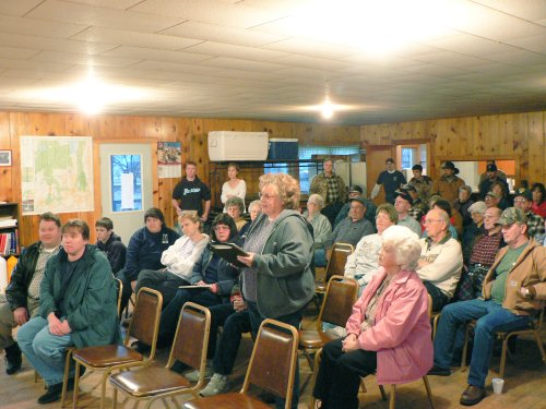 A crowd of at least 40 people seated in chairs at a public meeting.