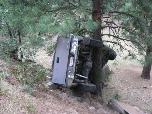 The silver pickup truck, on it's side against a tree.
