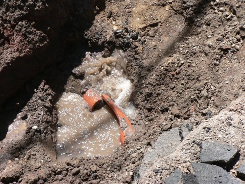 A terra cotta pipe in a hole with water gushing out of the ground.