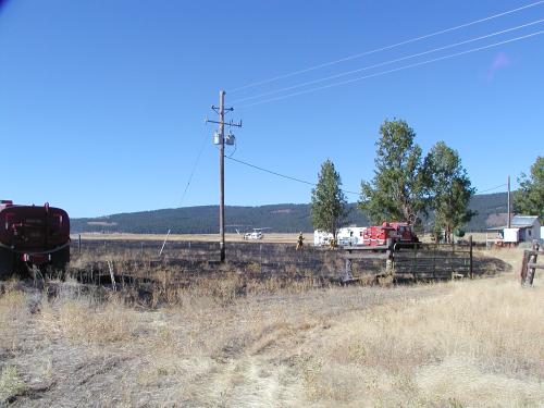 An open field with the last stages of a grass fire, firefighters and a CDF helicopter in the bacground on the ground.