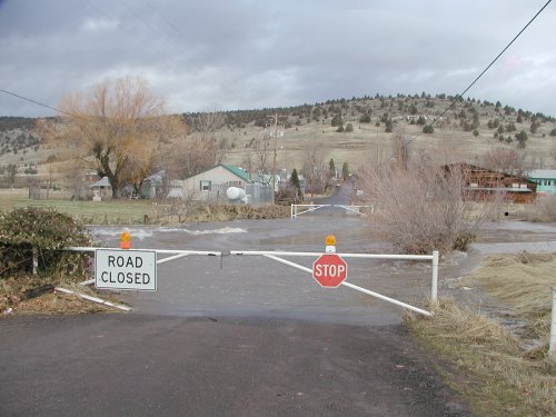 A road closed by a gate with "closed" sign and a swollen creek.