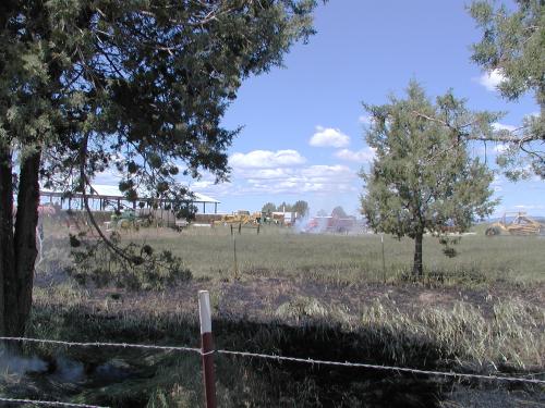 A fire truck in the distance near a smoking area of grass.