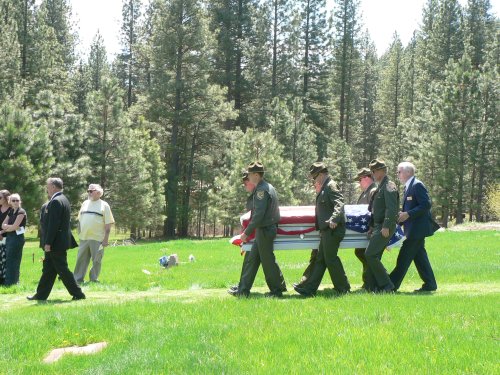 A flag draped casket carried by uniformed game wardens.