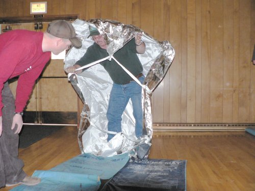 A man putting on an aluminum fire protectiion sheild while being watched by a trainer.