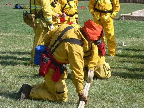 Yellow uniformed trainee firefighters practice rolling a hose