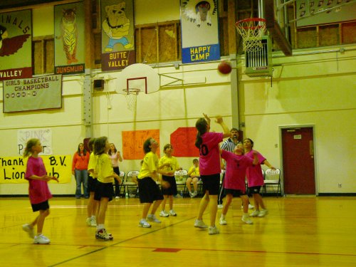 Girls in red and girls in yellow. Girl in red just shot a basket and ball is on the way up.