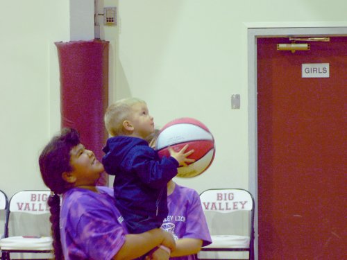A toddler being held up by a young lady player, trying to make a basket.
