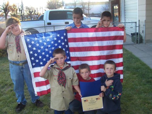 We see Cub Scouts in uniform saluting while displaying an American Flag.